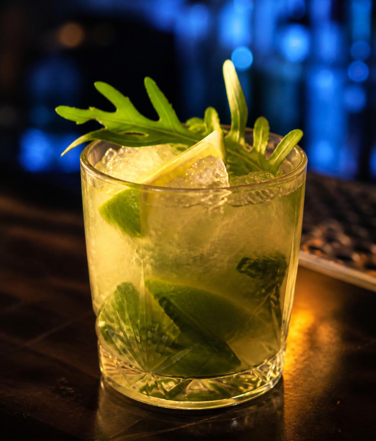 Caipirinha de rúcula com limão e gelo em copo baixo, sobre balcão de bar